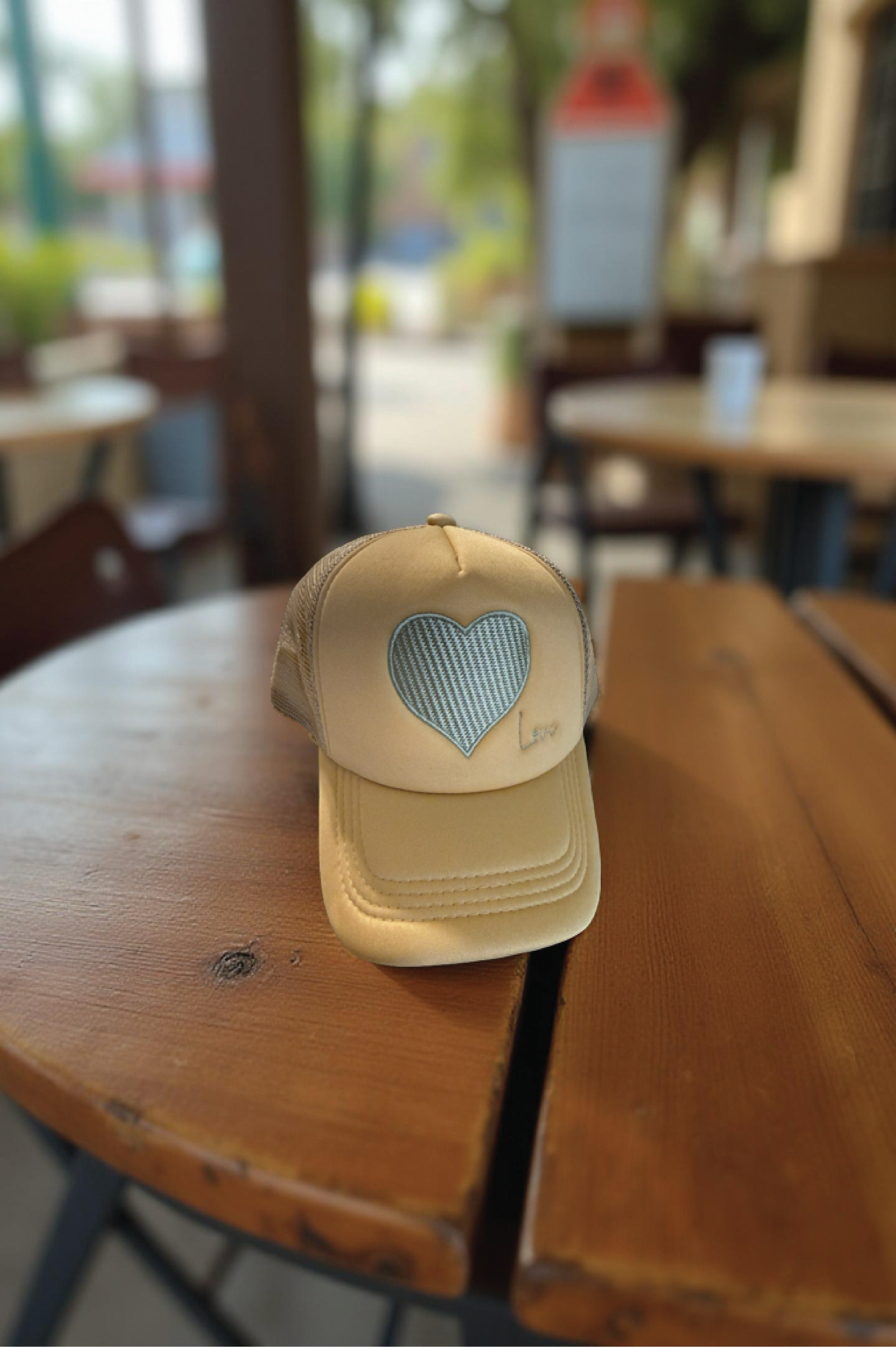 Beige cap with a heart-shaped cutout on a wooden table in an outdoor setting