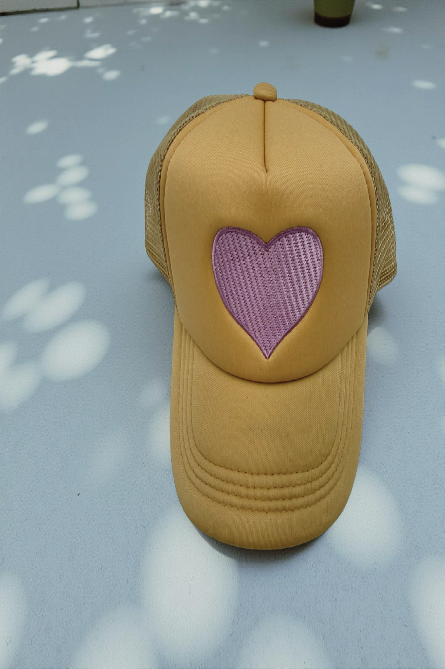 Beige cap with a pink heart design on a light gray surface