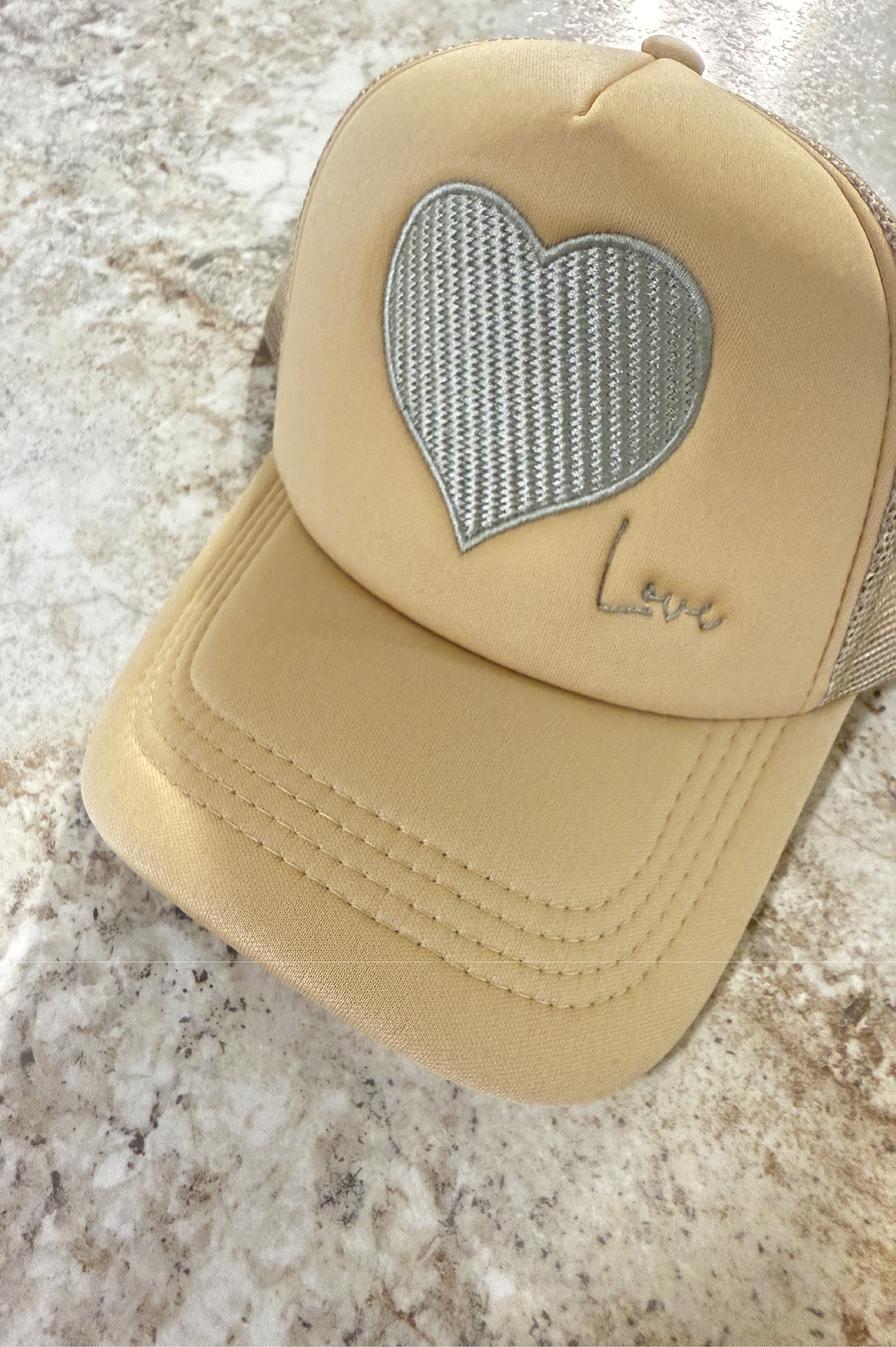 Beige cap with a heart-shaped mesh patch on a marble surface