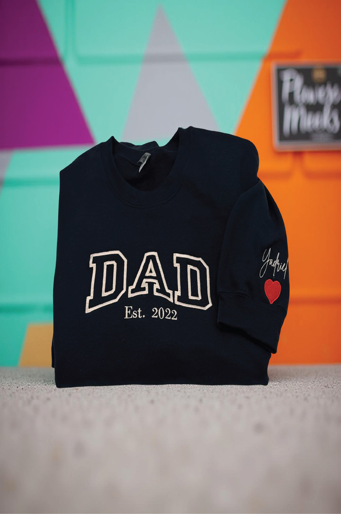 Black hoodie with 'DAD Est. 2022' text and a heart on a colorful background

Dad custom embroidered sweatshirt with kids’ names on sleeve – black pullover

Personalized dad sweatshirt with child name embroidered on sleeve – gray crewneck