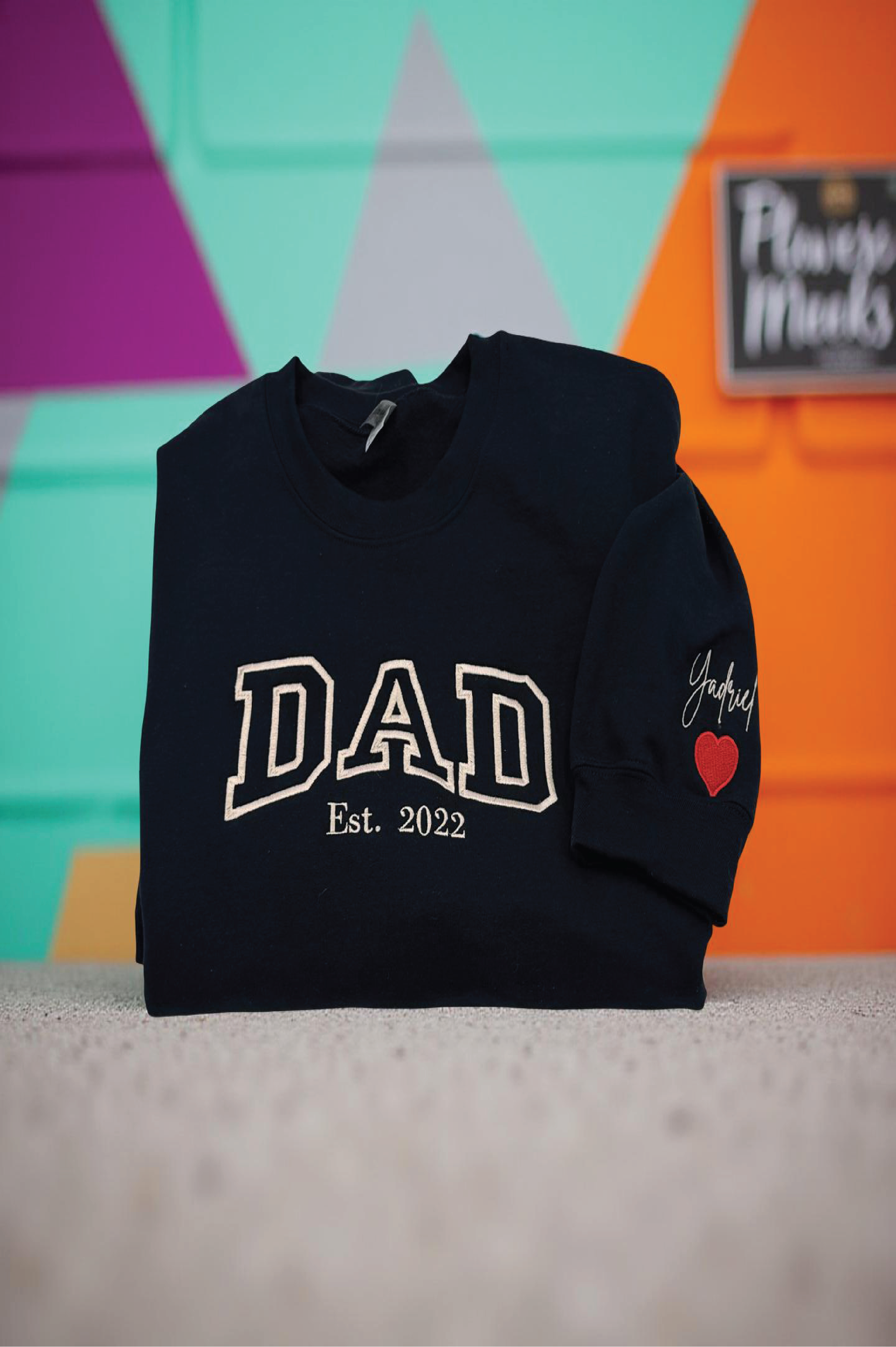 Black hoodie with 'DAD Est. 2022' text and a heart on a colorful background

Dad custom embroidered sweatshirt with kids’ names on sleeve – black pullover

Personalized dad sweatshirt with child name embroidered on sleeve – gray crewneck