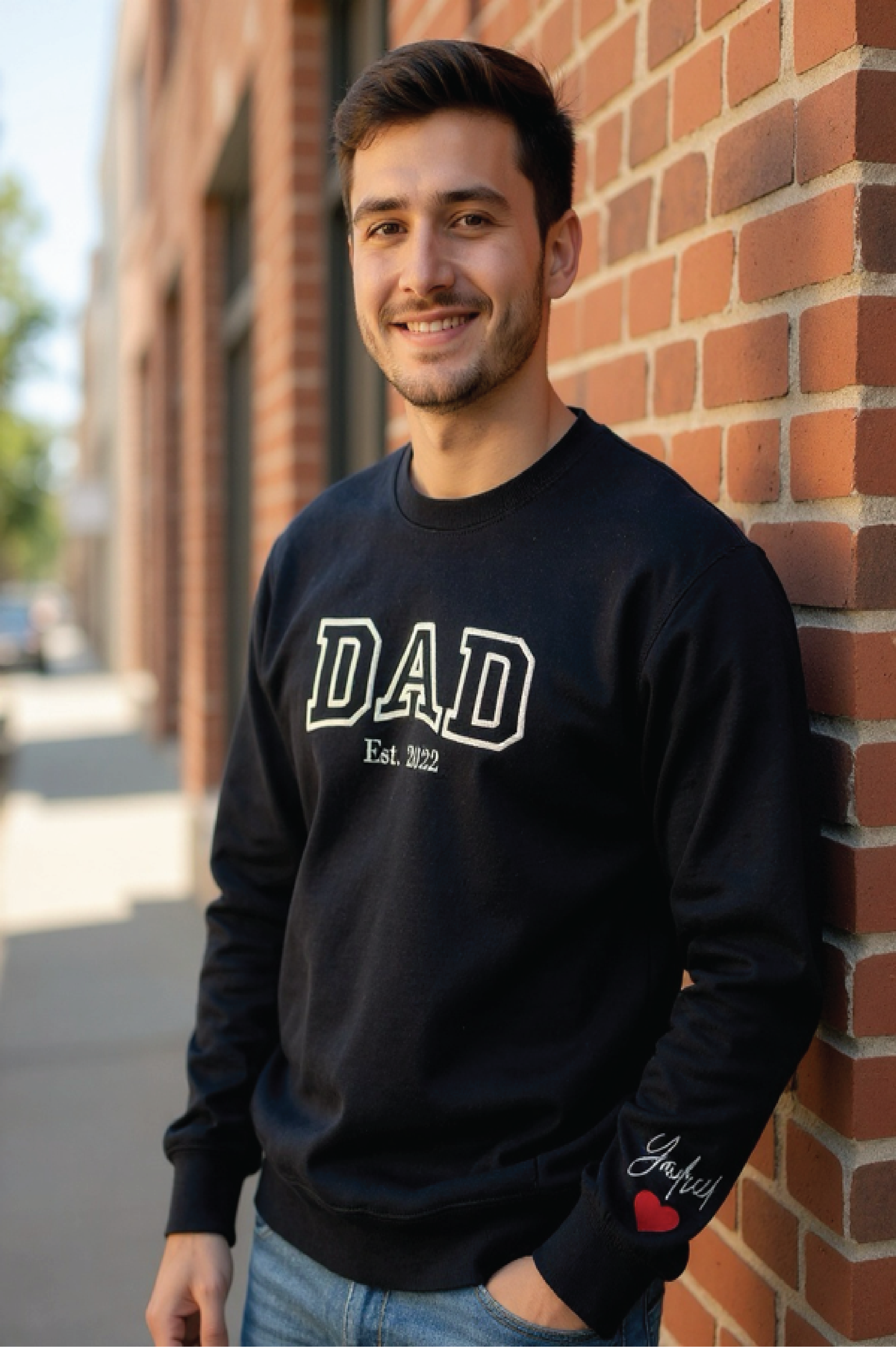 Man wearing a black sweatshirt with 'DAD' printed on it, standing against a brick wall.

Dad custom embroidered sweatshirt with kids’ names on sleeve – black pullover

Personalized dad sweatshirt with child name embroidered on sleeve – gray crewneck