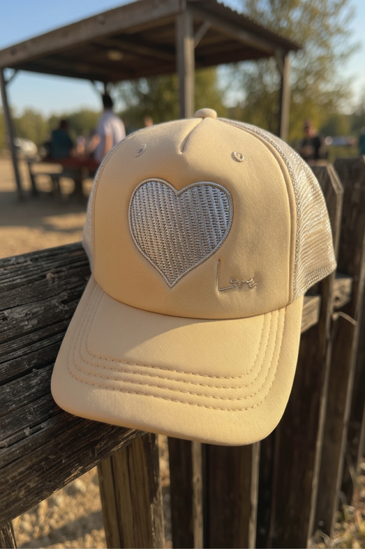 Beige cap with a heart-shaped mesh design on a wooden surface outdoors.