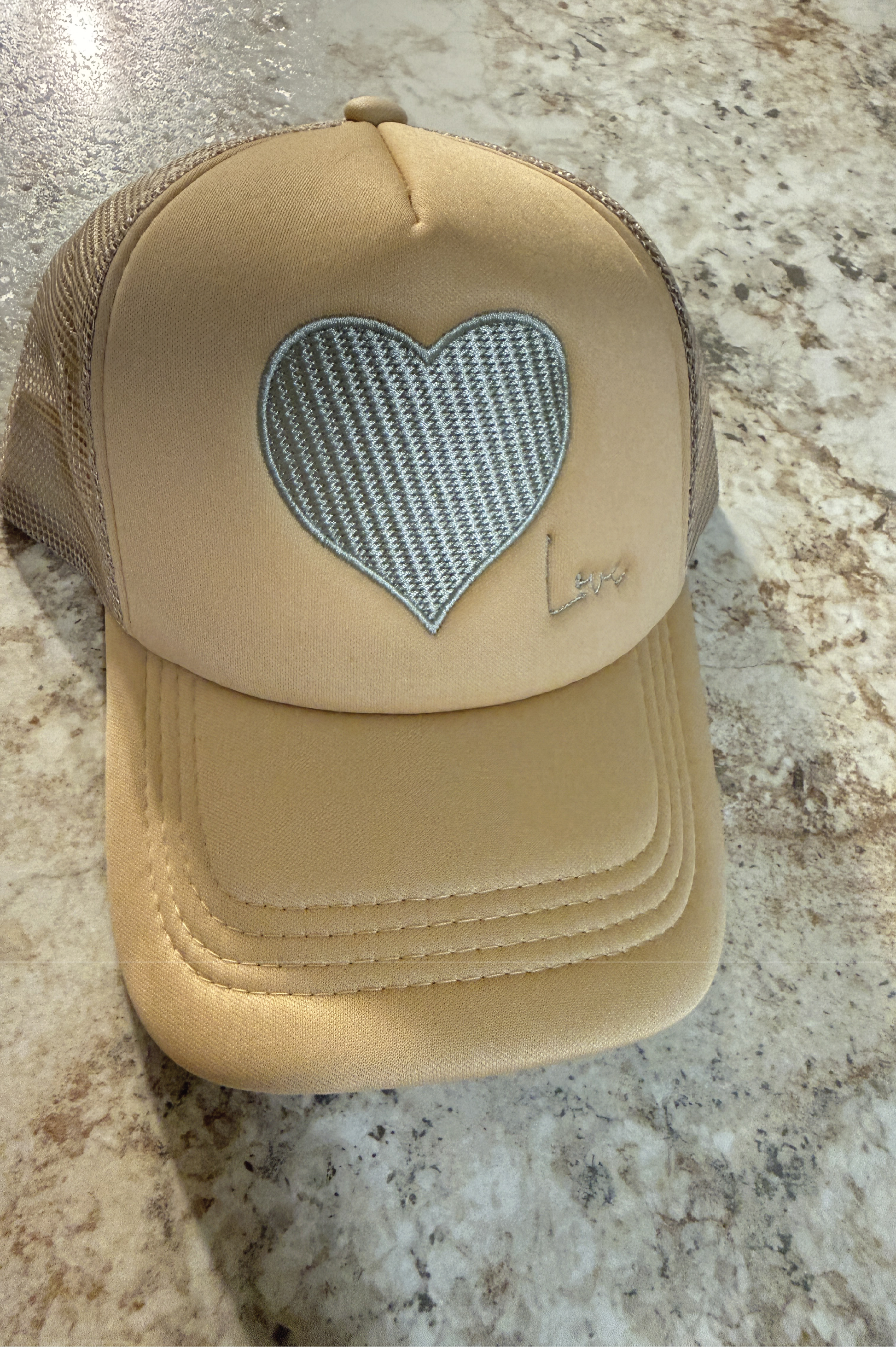 Beige cap with a heart-shaped mesh area on a marble surface